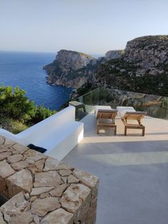 an outdoor area with chairs and tables overlooking the water's edge, near a cliff