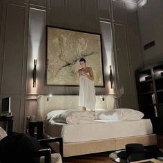 a woman standing on top of a bed in a room with gray walls and white furniture