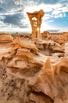 the sun shines through the clouds over some rocks and rock formations in the desert