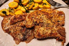 two pieces of meat on a white plate with lemons and spinach