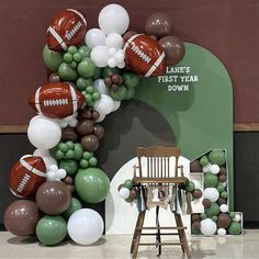 a balloon arch with footballs and balloons on the wall in front of a chair