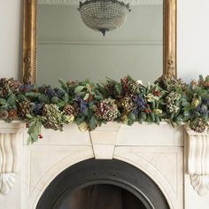 a fireplace decorated with greenery and pine cones for the mantel above it is a mirror