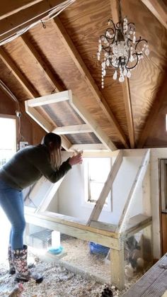 a woman standing on top of a wooden floor next to a chicken house with a chandelier hanging from the ceiling