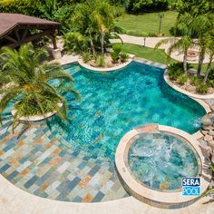 an aerial view of a swimming pool surrounded by palm trees and other greenery, with a gazebo in the background