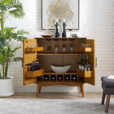 a wooden cabinet with wine glasses and bottles on it next to a potted plant