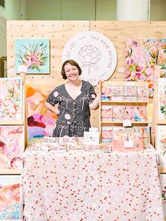 a woman standing in front of a table with paintings on it