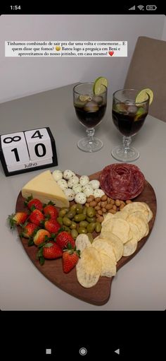 a wooden heart shaped platter filled with cheese, crackers and fruit