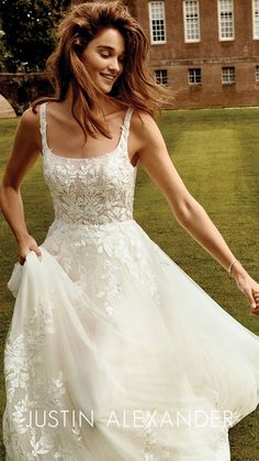 a woman in a wedding dress is walking through the grass with her hands behind her back