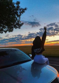 a person sitting on top of a car waving at the sun setting in the distance