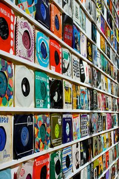 there are many records on the wall and one is in front of them, all different colors