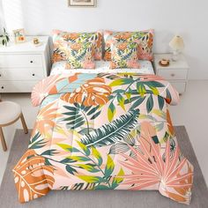 a bed with an orange and green tropical print on it, next to a white dresser