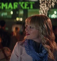 a woman standing in front of a store with lights on the building behind her smiling