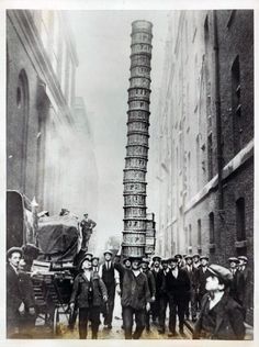 a group of men standing next to each other in front of a tall tower with many people around it