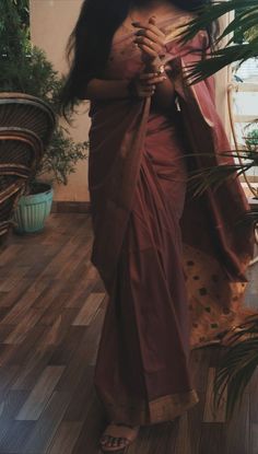 a woman in a red sari standing on a wooden floor next to a potted plant