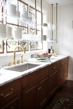 a kitchen with wooden cabinets and white counter tops, gold faucets on the window sill