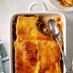 a casserole dish with meat and vegetables in it, next to a spoon