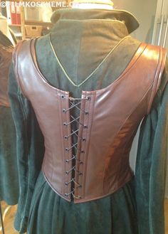 a green dress with brown leather details on the front and back, sitting on a mannequin's dummy