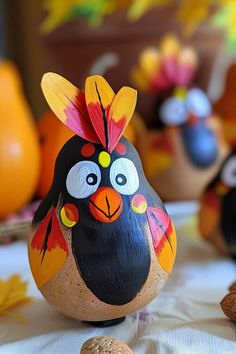 a painted bird sitting on top of a table next to nuts and orange pumpkins