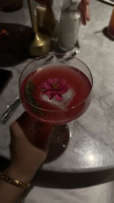 a close up of a person holding a wine glass with a flower in it on a table