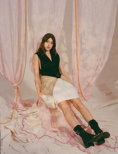 a woman sitting on top of a white sheet next to pink drapes and curtains