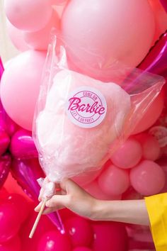 a person holding a lollipop in front of pink and white balloons with the word barbie on it