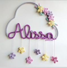 a crocheted name sign hanging from the side of a wall with flowers on it