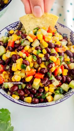 a hand dipping a tortilla chip into a bowl of black bean and corn salad