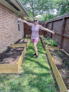 a woman in pink shirt and shorts standing next to garden beds