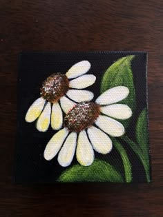 a painting of three white daisies on a black square with green leafy stems