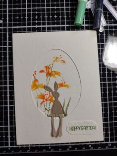 a card with an image of a rabbit and flowers in the center, surrounded by crafting supplies