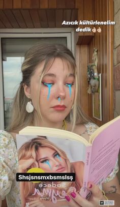 a girl with blue eyes reading a book in front of her face and looking at the camera