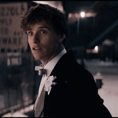 a man in a tuxedo and bow tie looking at the camera while standing outside