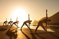 a group of people doing yoga on a dock at sunset with the sun in the background