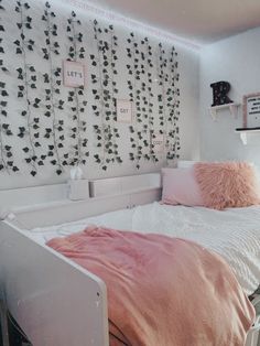 a white bed sitting under a window next to a wall covered in pink and black leaves