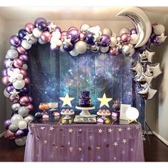 a purple and white dessert table with stars, balloons and cake on it in front of a backdrop