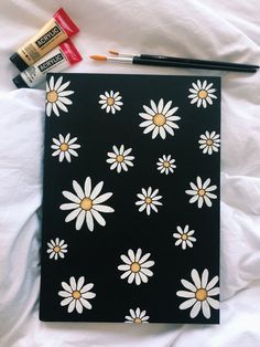 a black notebook with white daisies on it and some markers next to it,