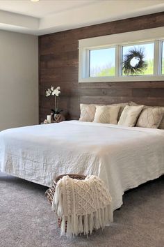 a large white bed sitting in a bedroom next to a window on top of a wooden headboard