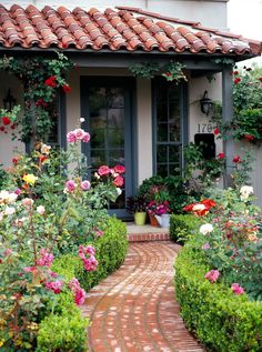 a brick pathway leading to a house with roses growing on it