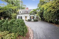 a white house surrounded by trees and shrubbery in front of it is an asphalt driveway