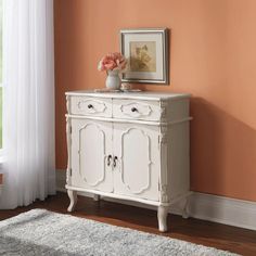 a white cabinet with flowers on top in front of an orange wall and carpeted floor