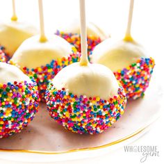 cake pops with white frosting and sprinkles on a gold rimmed plate