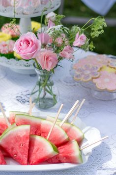 watermelon slices on skewers in front of pink roses and other flowers