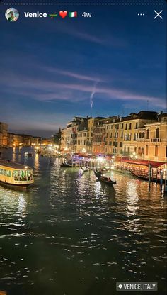 boats are floating in the water near buildings and lights at night, with an italian flag over them