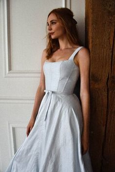 a woman in a white dress leaning against a wall