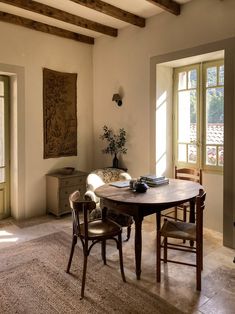 a table and chairs in a room with wooden beams on the ceiling, near two windows