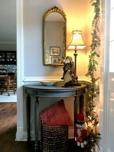 a table with a basket under it next to a lamp and mirror on the wall