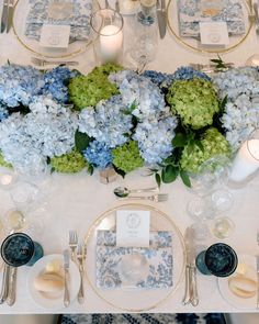 the table is set with blue and white plates, silverware, and hydrangeas