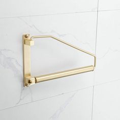 a gold triangle shaped towel ring on a white wall with marble tiles in the background