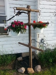 an old wooden cross with flowers on it in front of a house