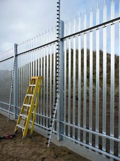 a yellow ladder leaning against a fence next to a white metal fence with bars on it